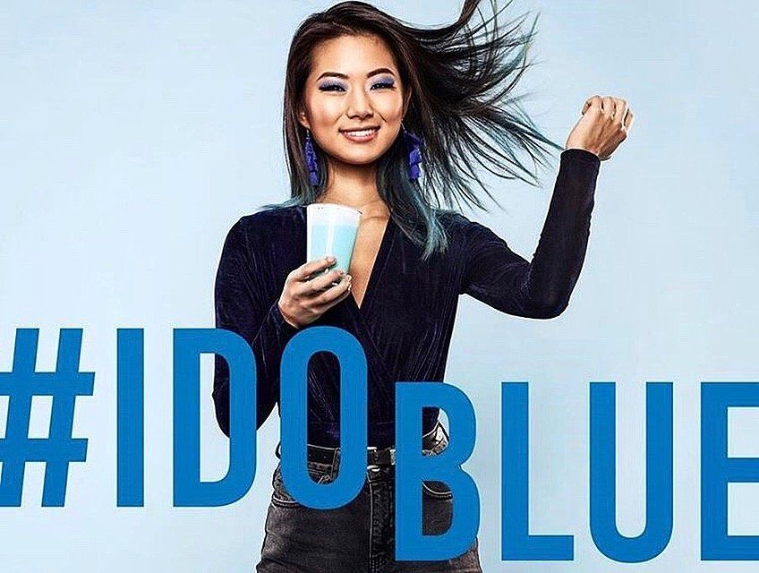 A woman with blue hair is holding a cup in her hand.