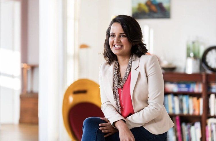 A woman is sitting on a chair in a living room and smiling.