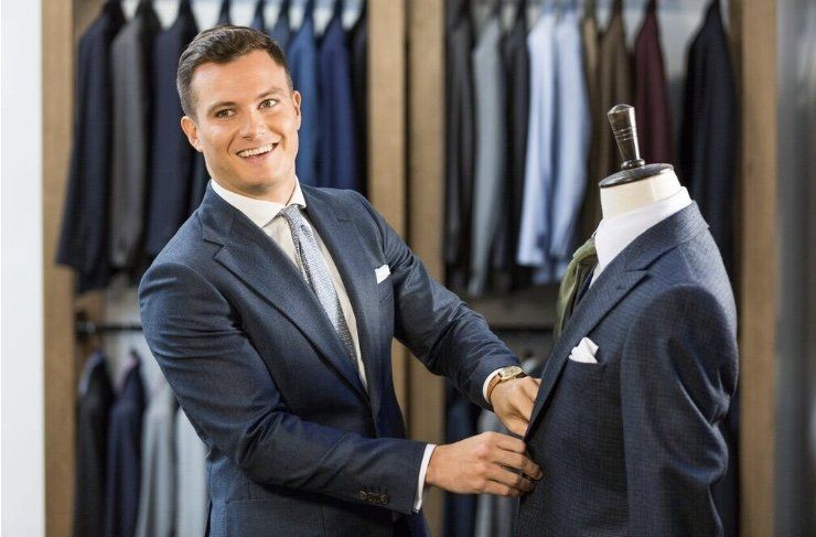 A man in a suit is adjusting a suit on a mannequin.