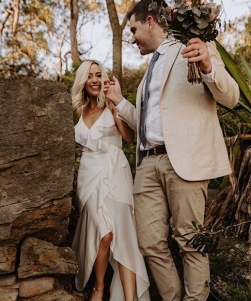 A bride and groom are standing next to each other holding a bouquet of flowers.