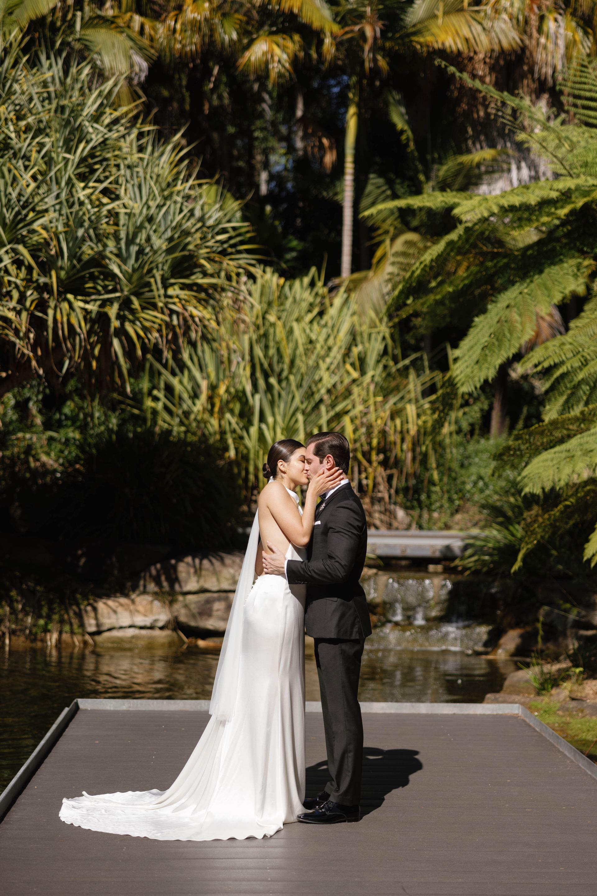 bride kisses groom by the water. Hair and makeup still perfect.