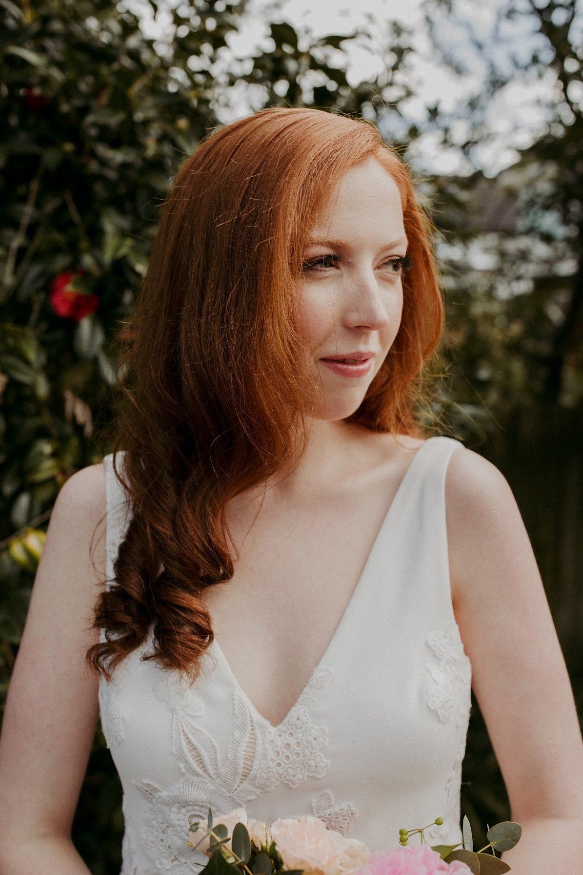 A woman with red hair is wearing a white dress and holding a bouquet of flowers.
