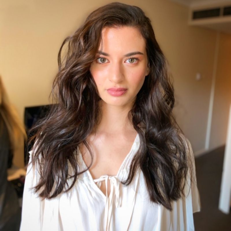 A woman with long brown hair is wearing a white shirt