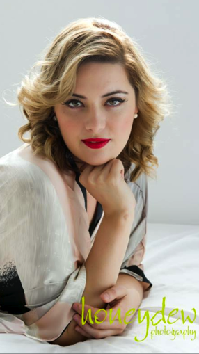 A woman is laying on a bed with her hand on her chin.