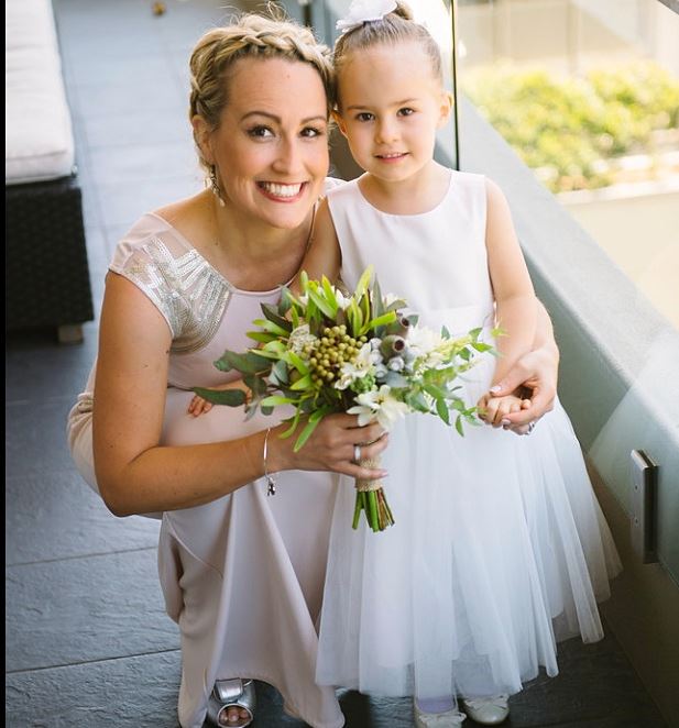 A woman is kneeling next to a flower girl who is holding a bouquet of flowers