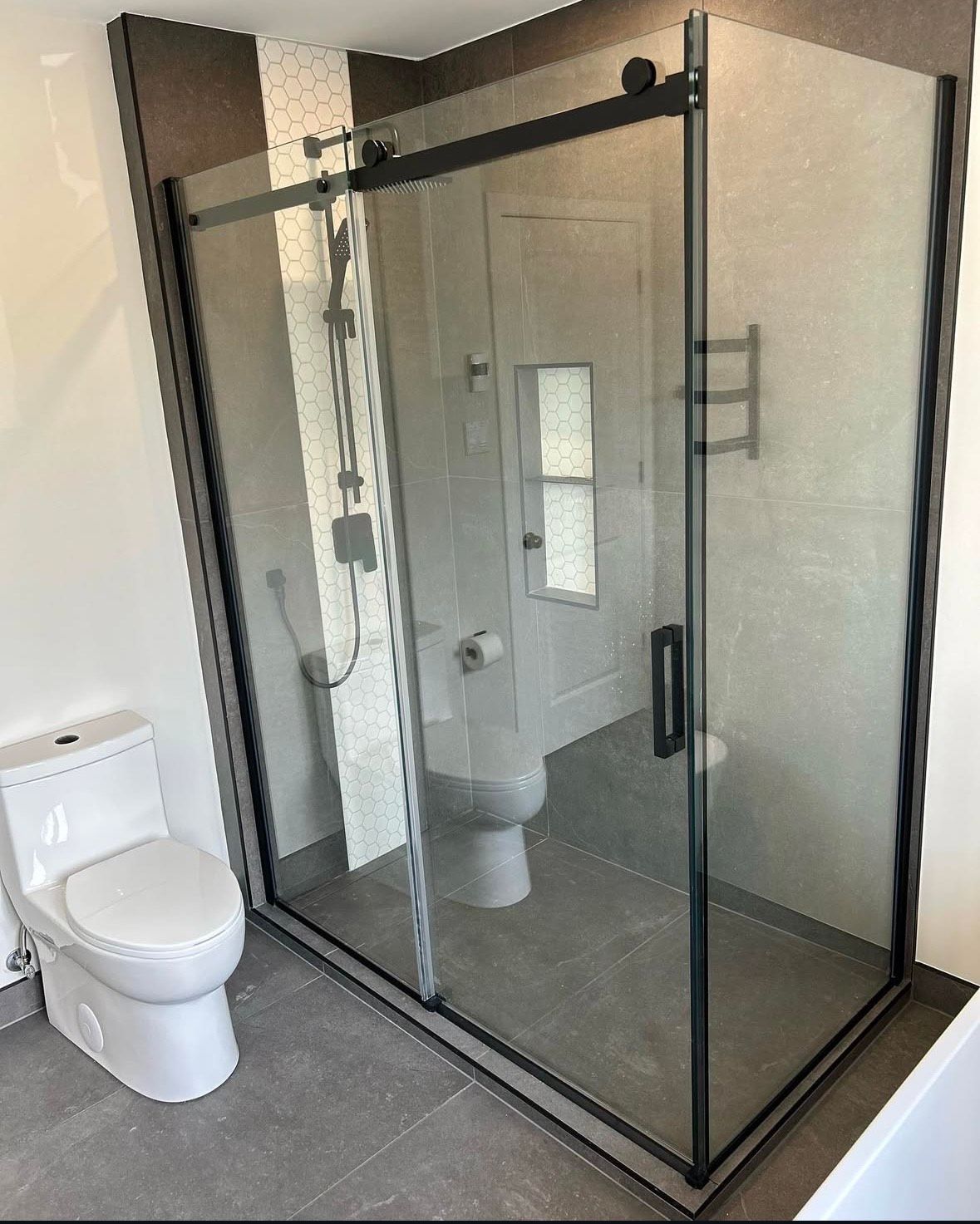 A bathroom with a toilet and a shower stall with sliding glass doors.