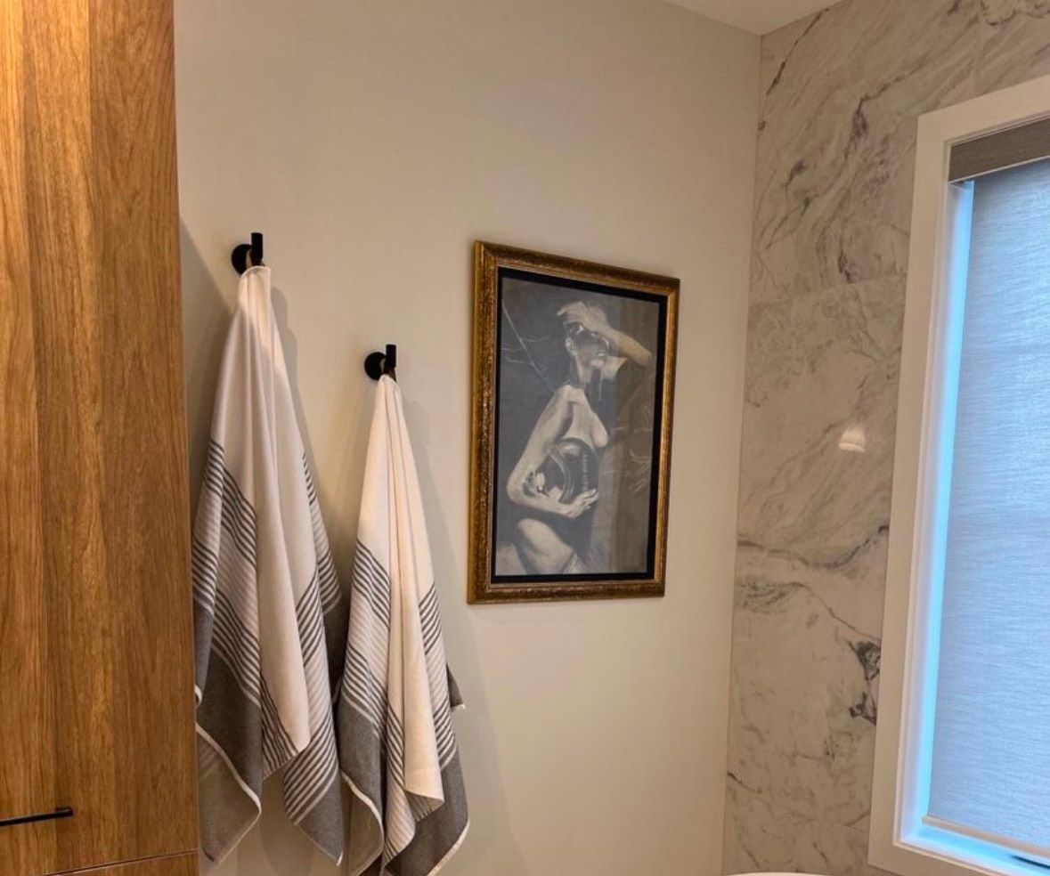 Une salle de bain avec des serviettes accrochées à des crochets et un tableau sur le mur.