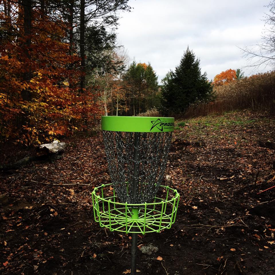A green disc golf goal in front of a Connecticut fall landscape.