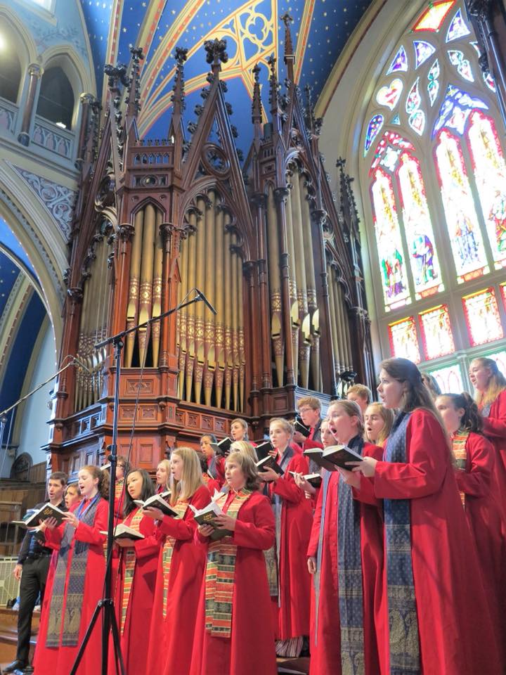 A choir is singing in a church in front of an organ.