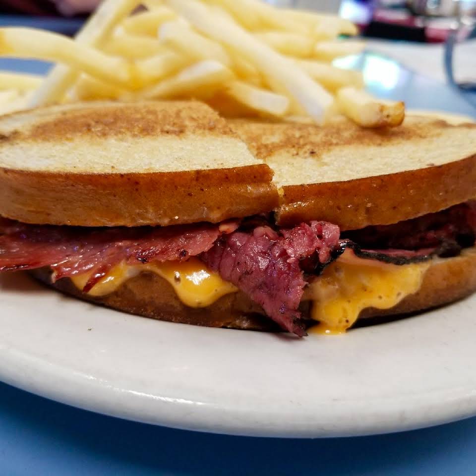 A sandwich on a white plate with french fries in the background
