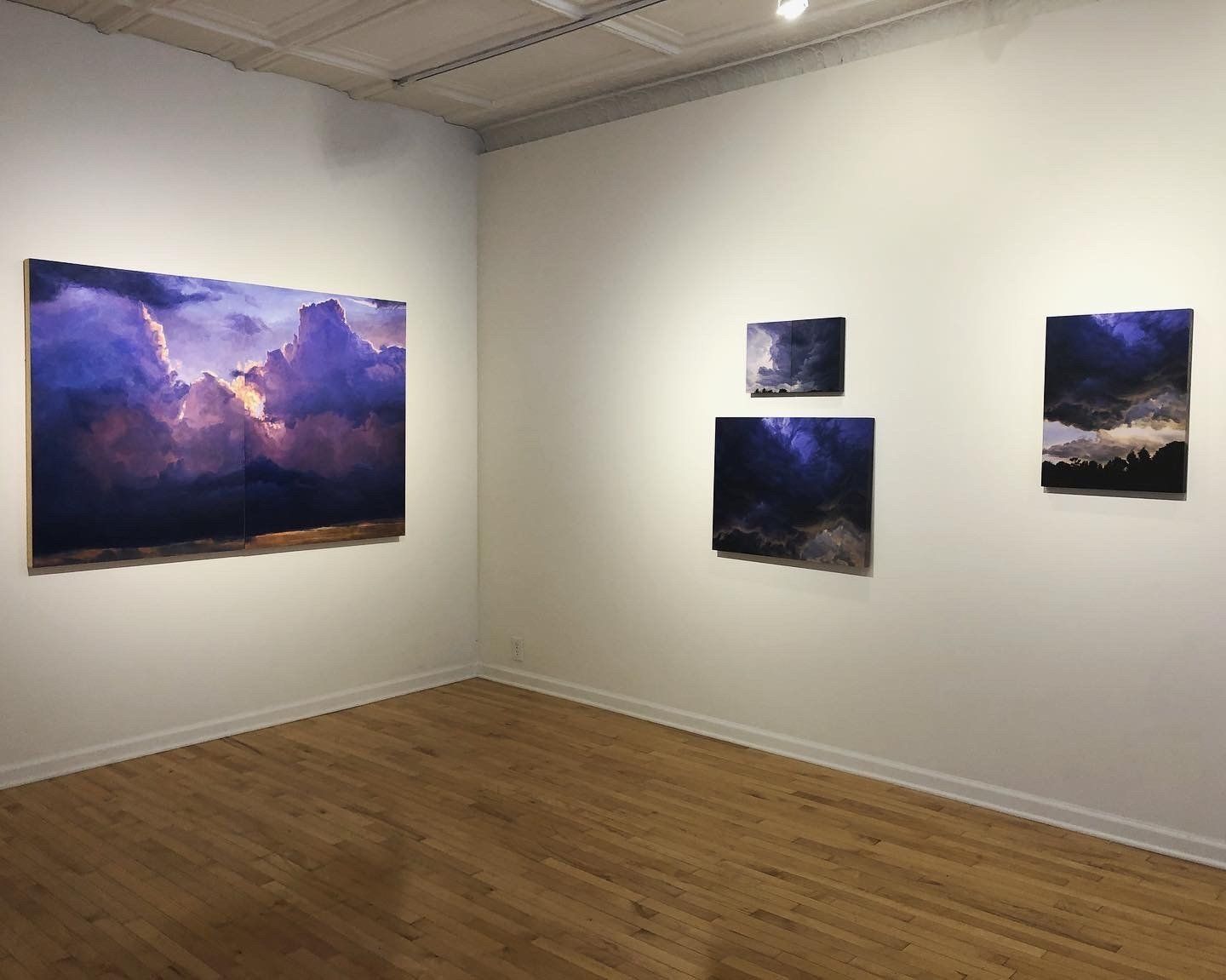 A room with three paintings on the wall and a wooden floor.