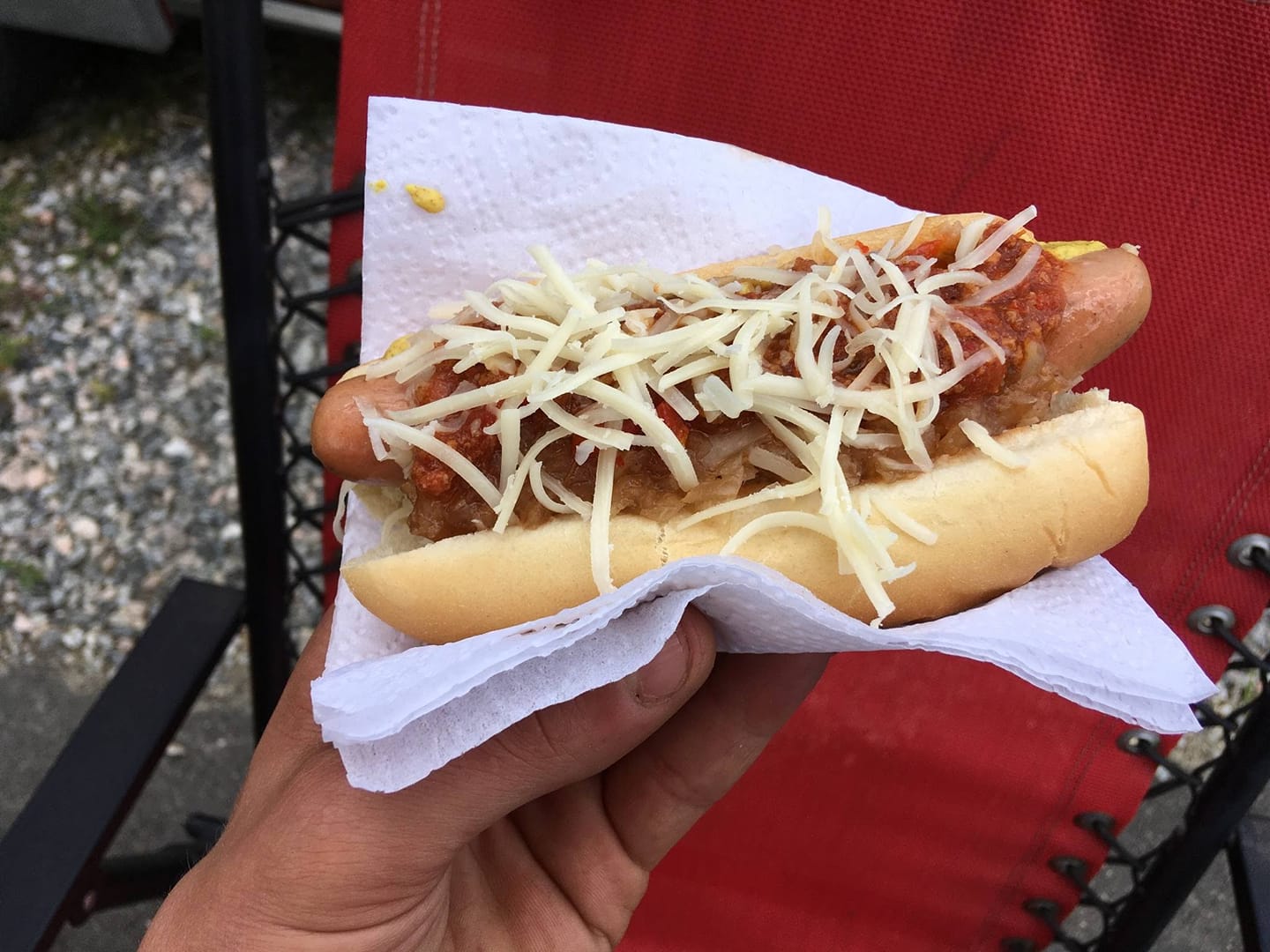 A person is holding a hot dog with sauce and cheese on a napkin.