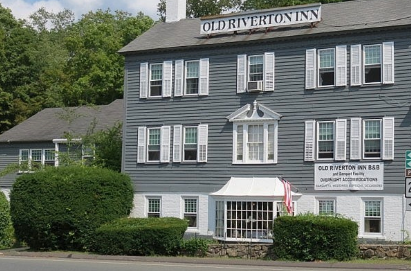 A gray building with white shutters and a sign that says old riverton inn