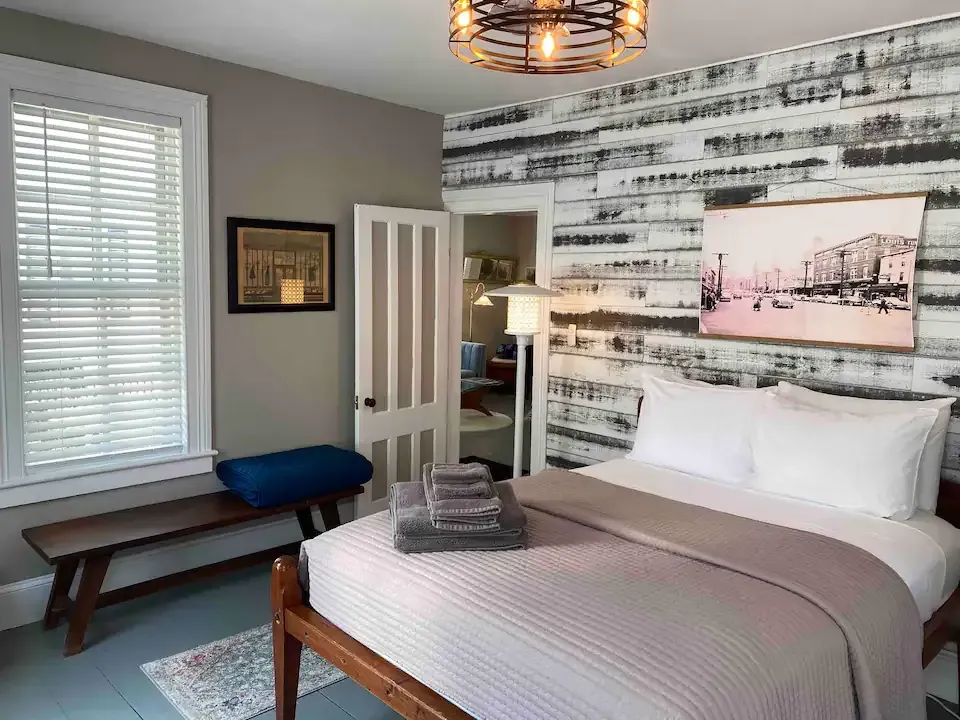 A bedroom with a bed , window , bench and painting on the wall.