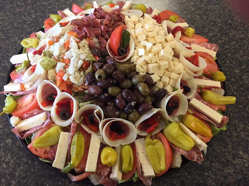 A tray filled with meats , cheeses , olives and peppers on a table.