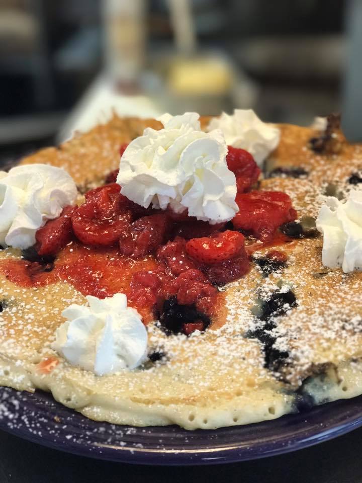 A pancake with whipped cream and strawberries on top
