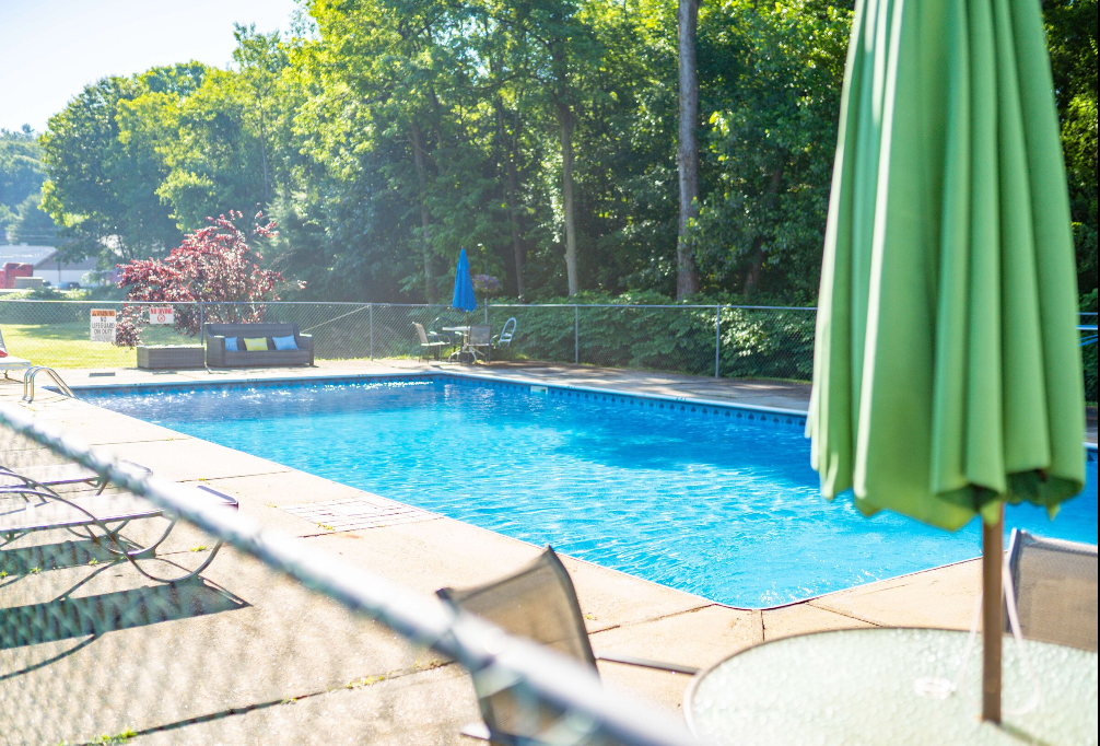 A large swimming pool with a green umbrella and chairs
