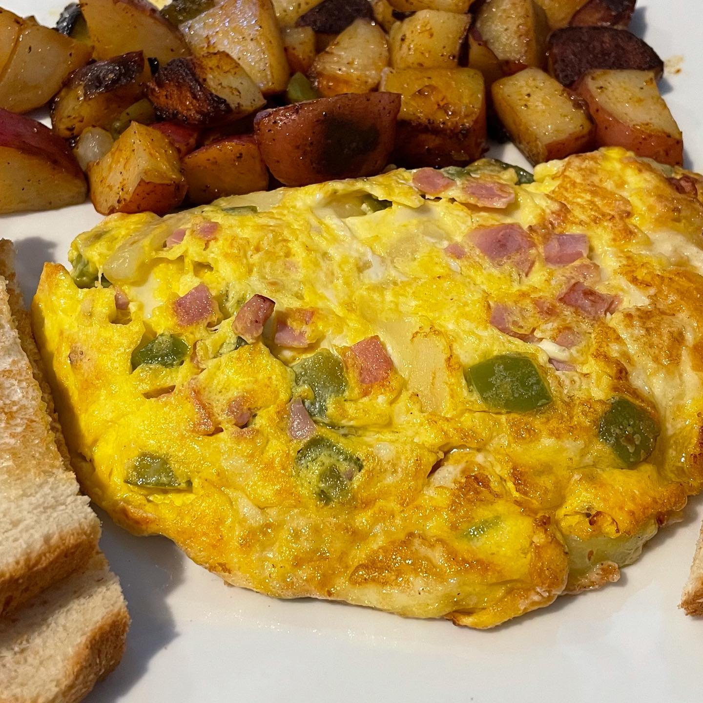 A close up of an omelet with potatoes and toast on a plate.