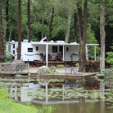 A rv parked in the woods next to a pond