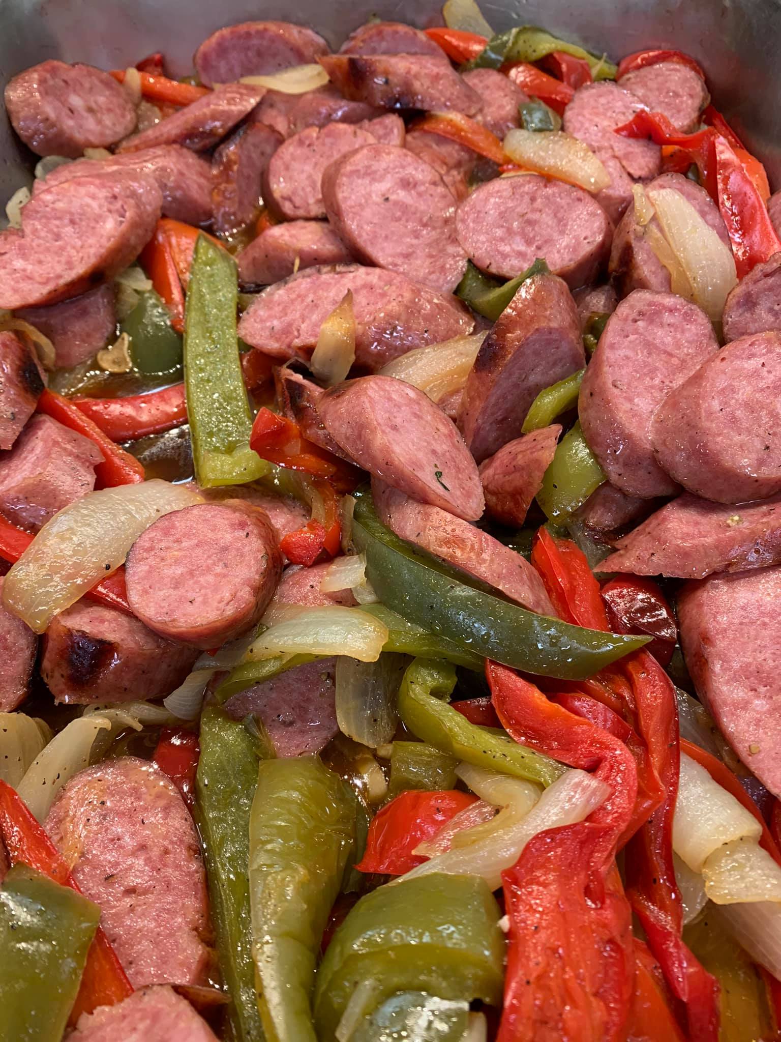 A close up of a casserole dish filled with sausage , peppers , onions and other vegetables.