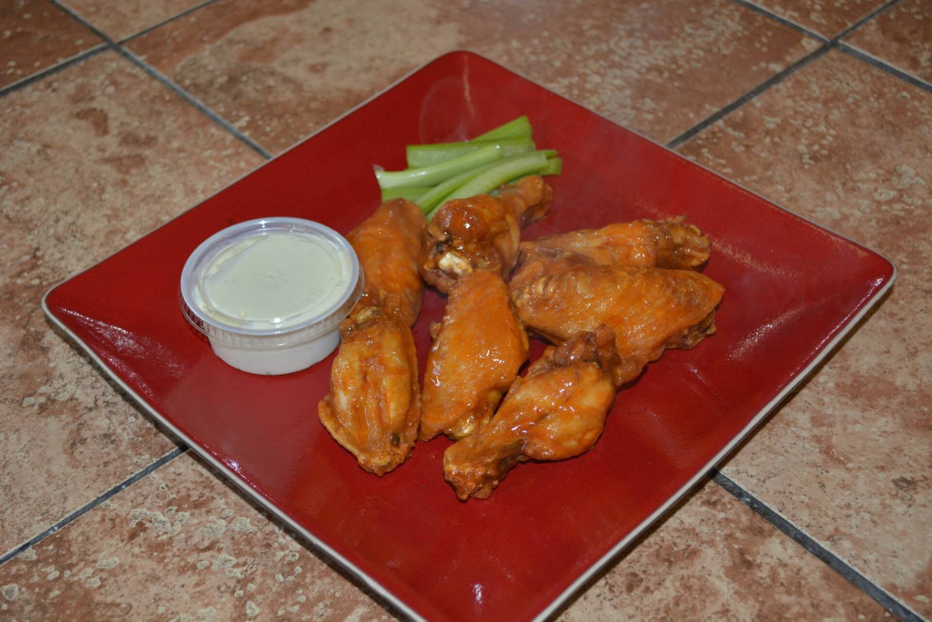 A red plate topped with chicken wings , celery and ranch dressing.