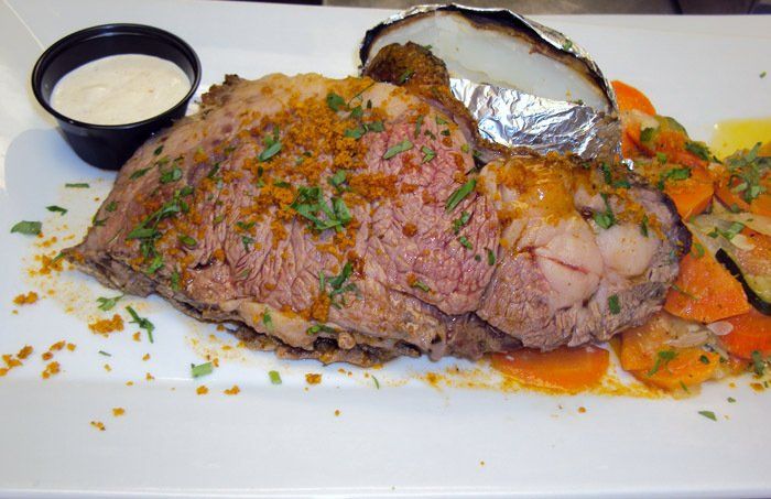 A white plate topped with a large piece of meat and vegetables.
