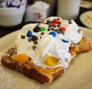 A close up of a piece of french toast with whipped cream and m & ms on a plate.
