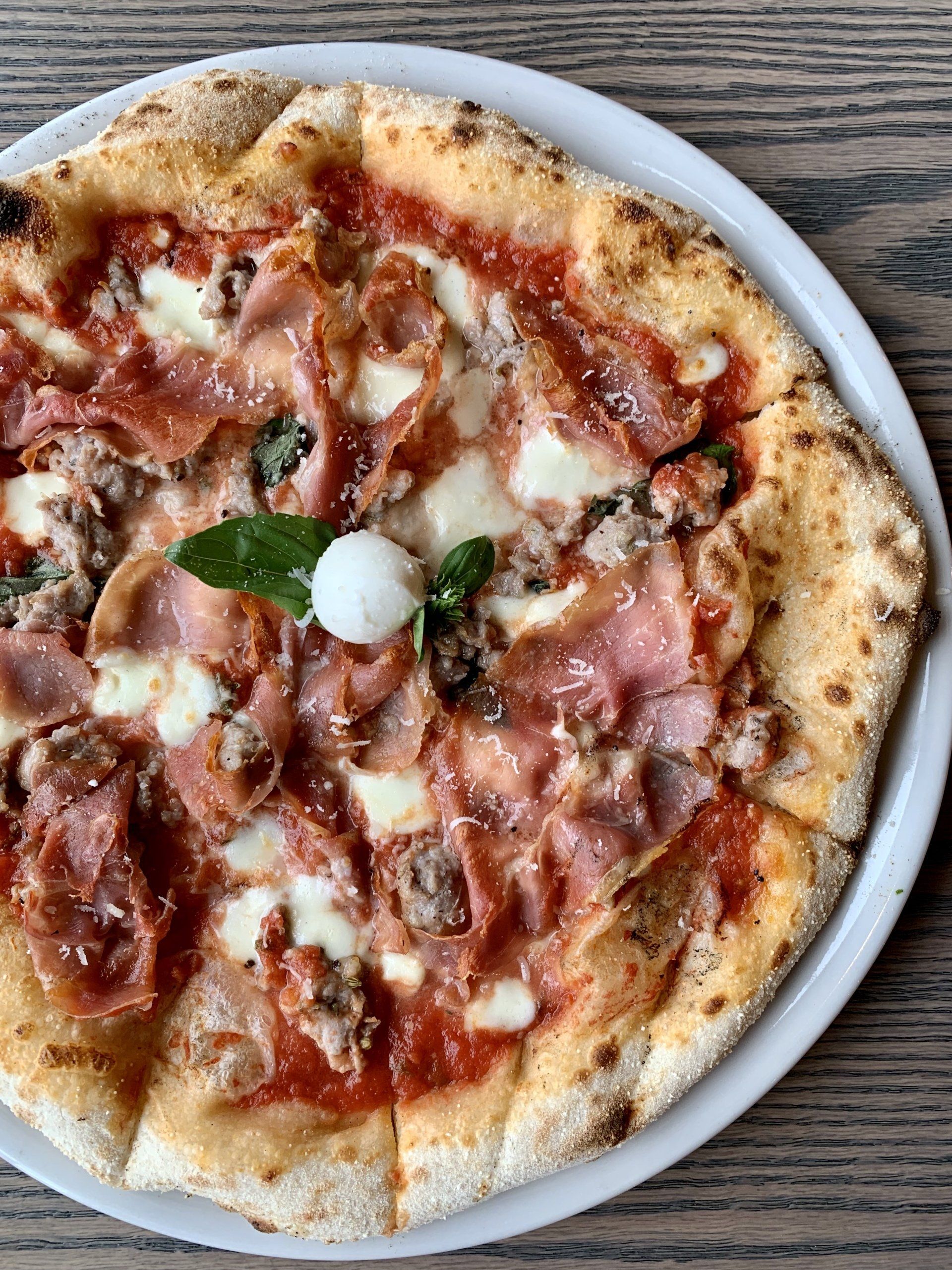 A pizza on a white plate on a wooden table.