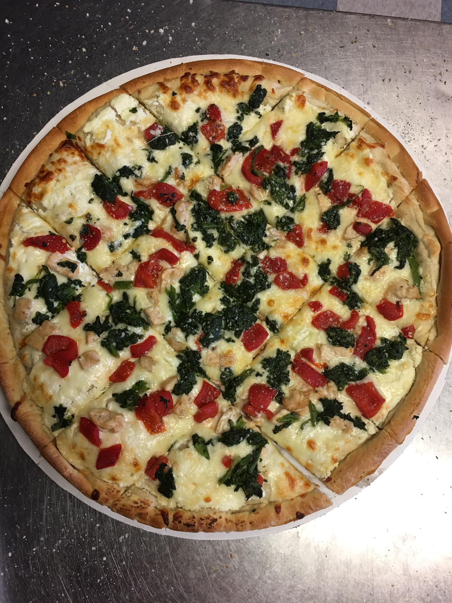 A pizza with spinach , tomatoes and cheese on a white plate.