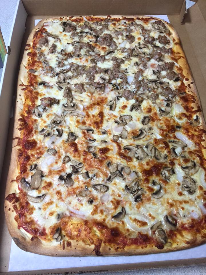 A large pizza with mushrooms , sausage and cheese is in a cardboard box.