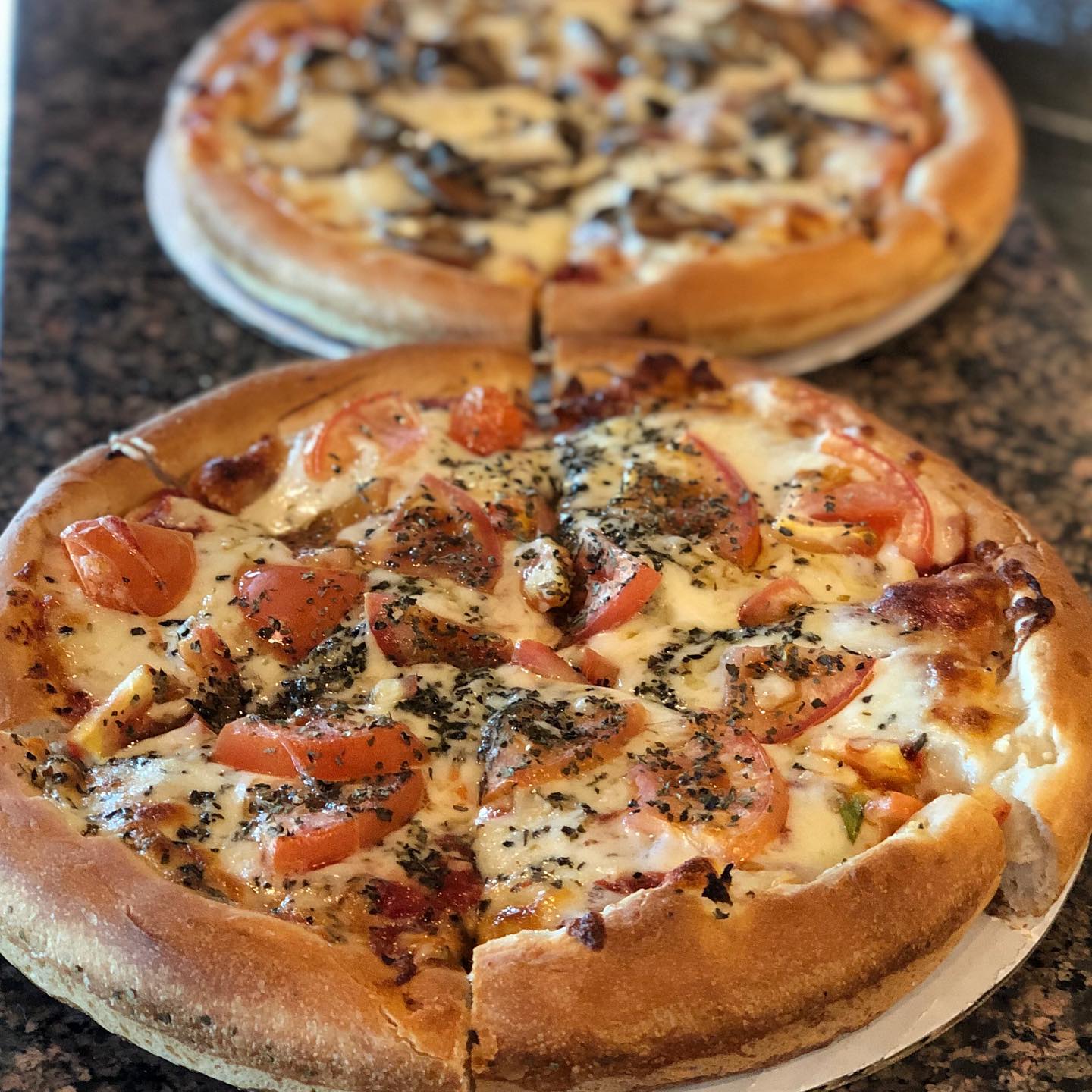 Two pizzas with tomatoes , cheese and mushrooms are on a table.