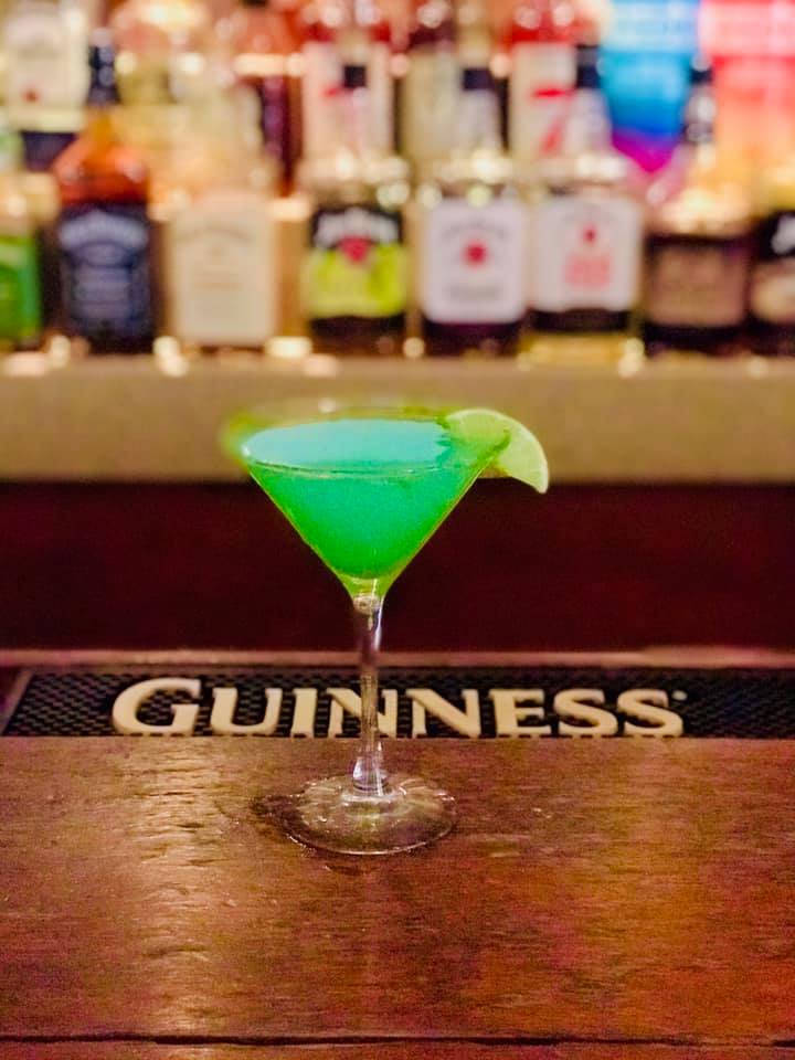 A green martini is sitting on a bar next to a guinness sign.