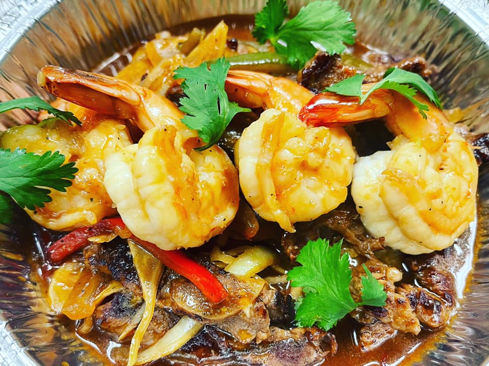 A close up of a foil container filled with shrimp and beef.