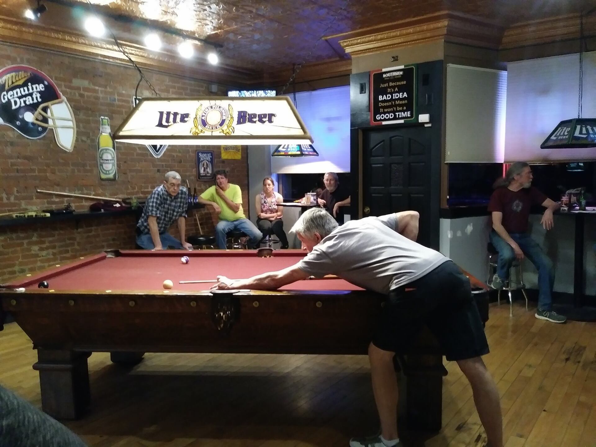 A man is playing pool in a bar under a lite beer light