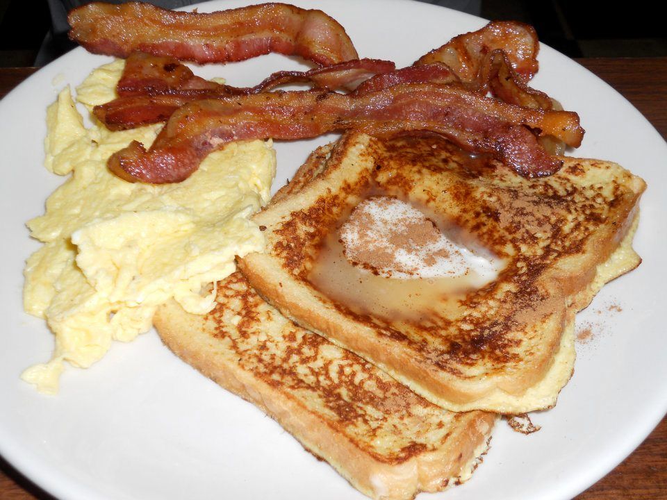 A white plate topped with french toast bacon and scrambled eggs