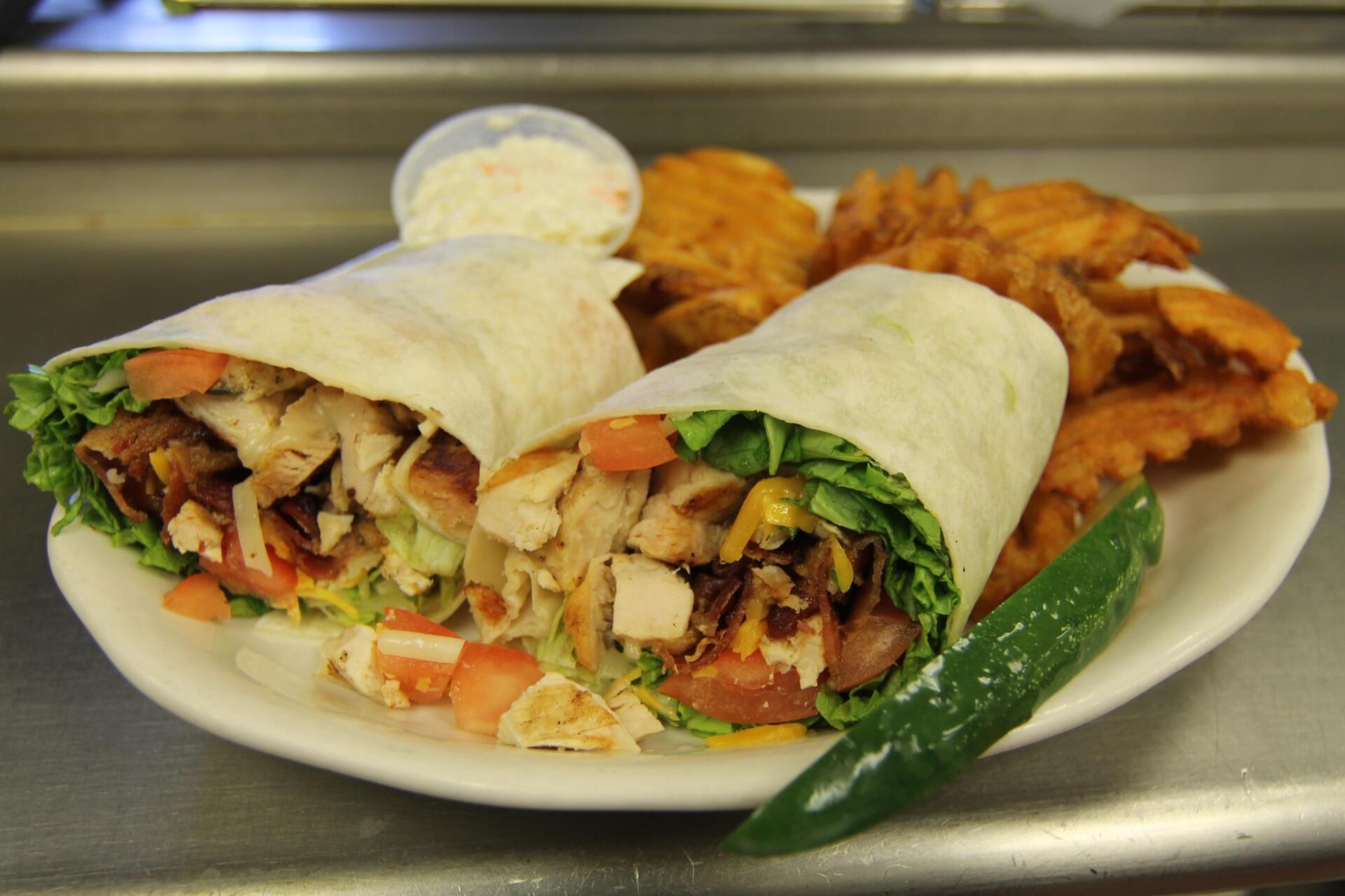 A white plate topped with a chicken wrap and waffle fries.