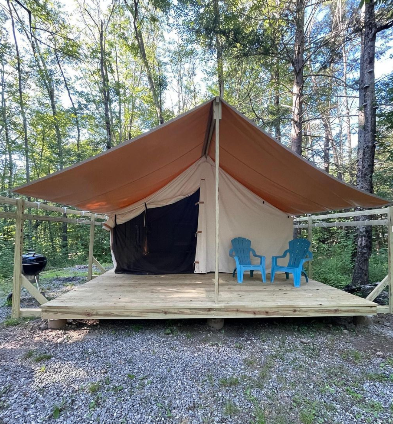 A tent with two blue chairs underneath it in the woods