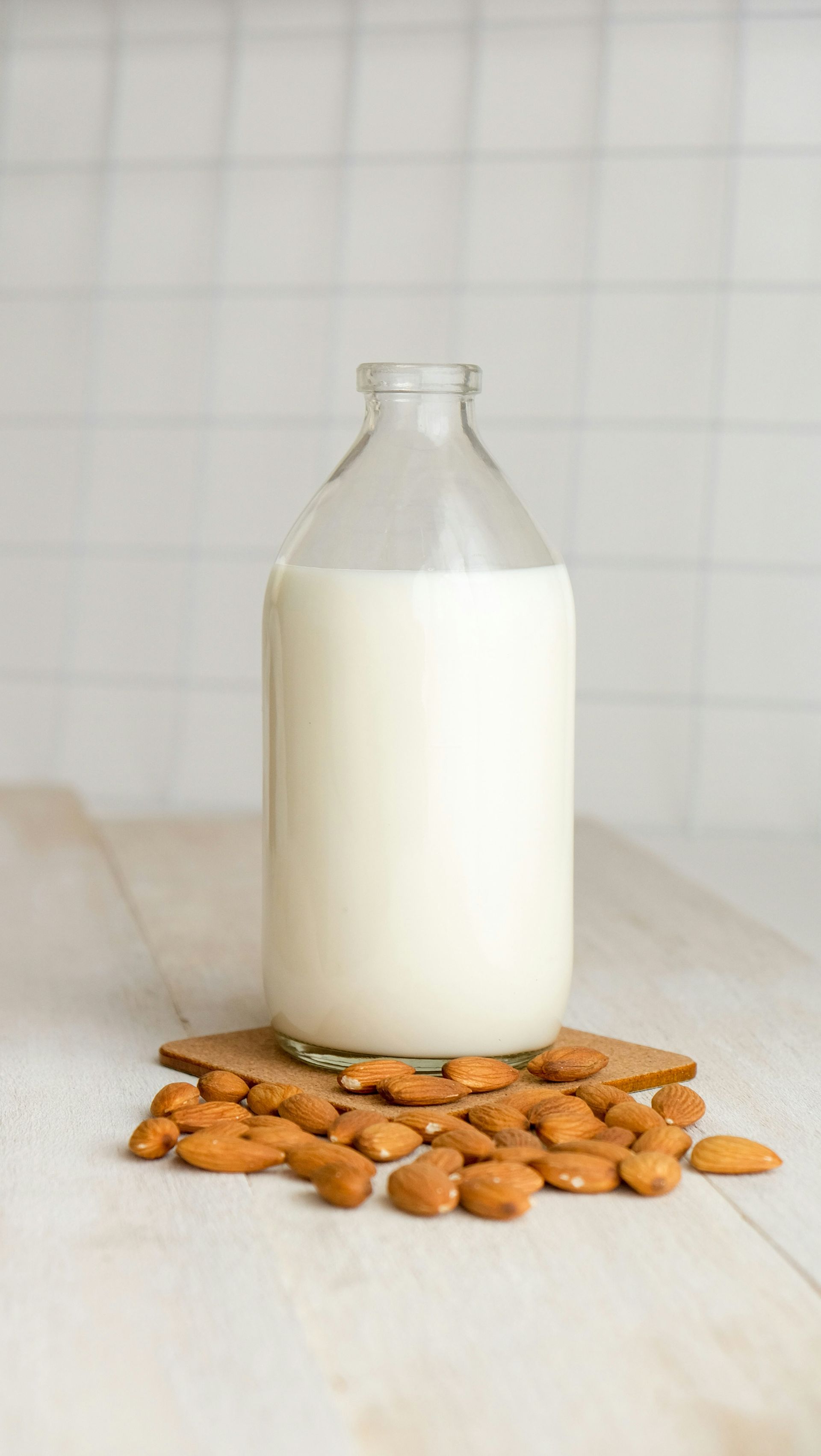A bottle of almond milk is sitting on a table next to almonds.