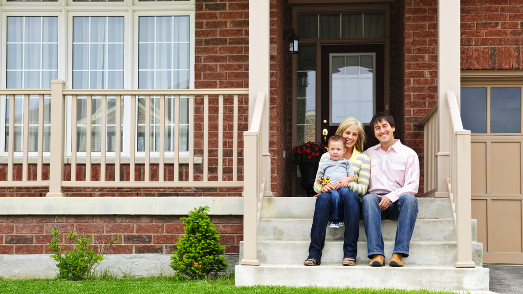 a family is sitting on the steps of their house .