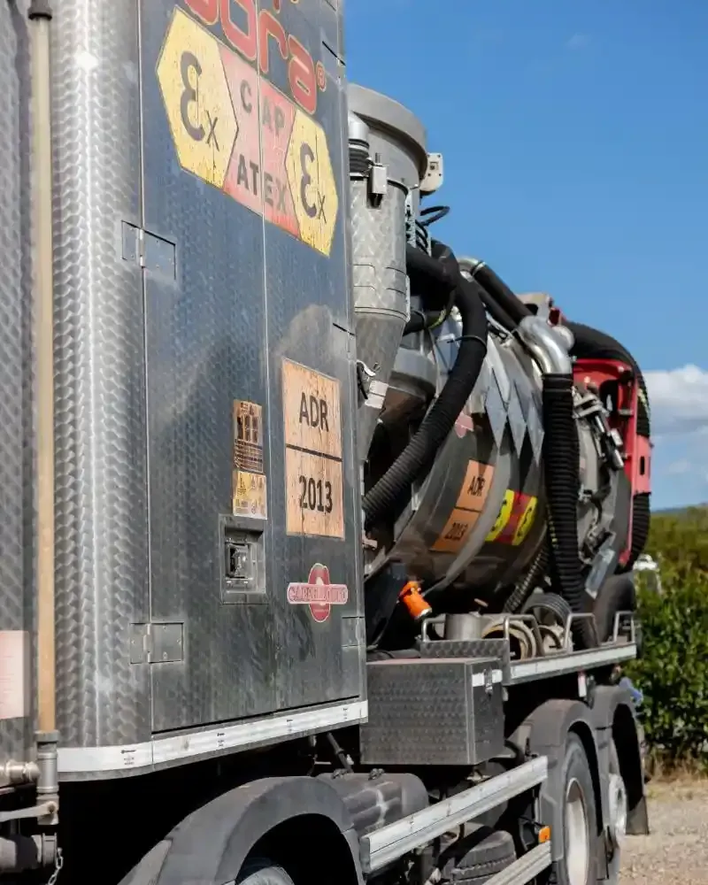 Un camion con fossa settica blu e bianca parcheggiato fuori da un edificio con tubi flessibili e comandi.