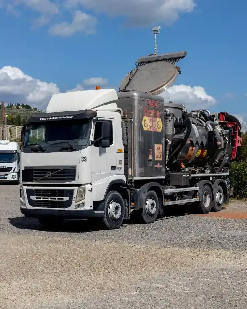 Autocarro con cassone ribaltabile bianco parcheggiato all'interno di un garage; ha un grande contenitore argentato per il trasporto dei materiali.