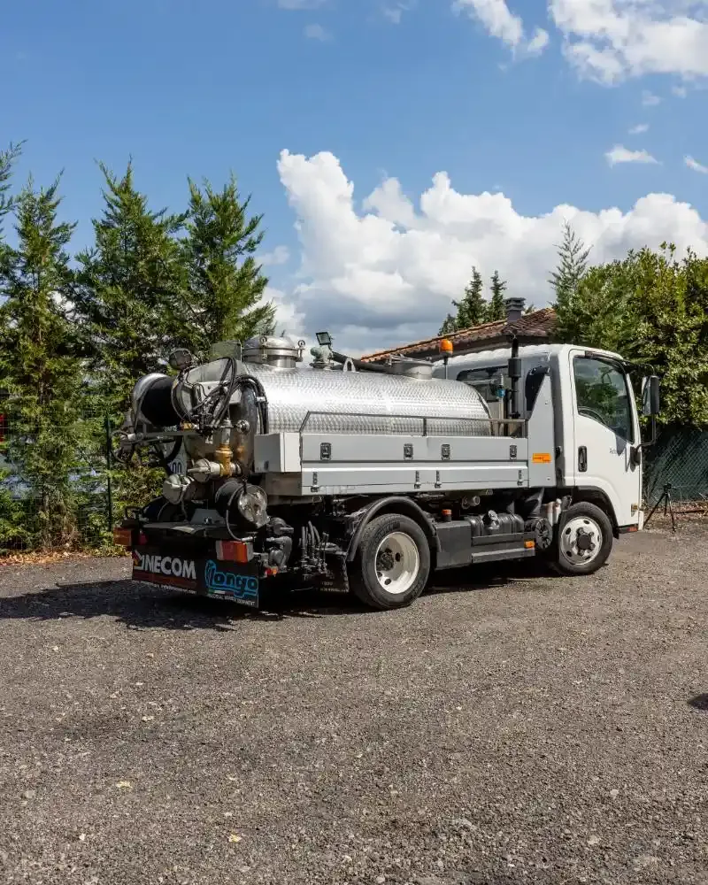Un camion della nettezza urbana blu e bianco parcheggiato accanto a un edificio beige chiaro.