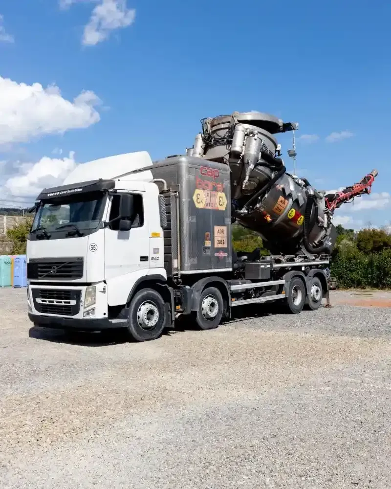 Uomo che tiene in mano un tubo flessibile collegato allo scarico fognario, sullo sfondo un camion aspiratutto blu.