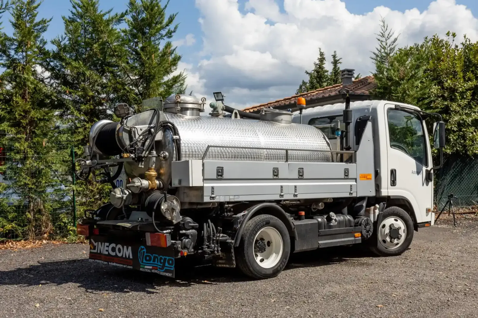 Un camion con fossa settica blu e bianca parcheggiato fuori da un edificio con tubi flessibili e comandi.