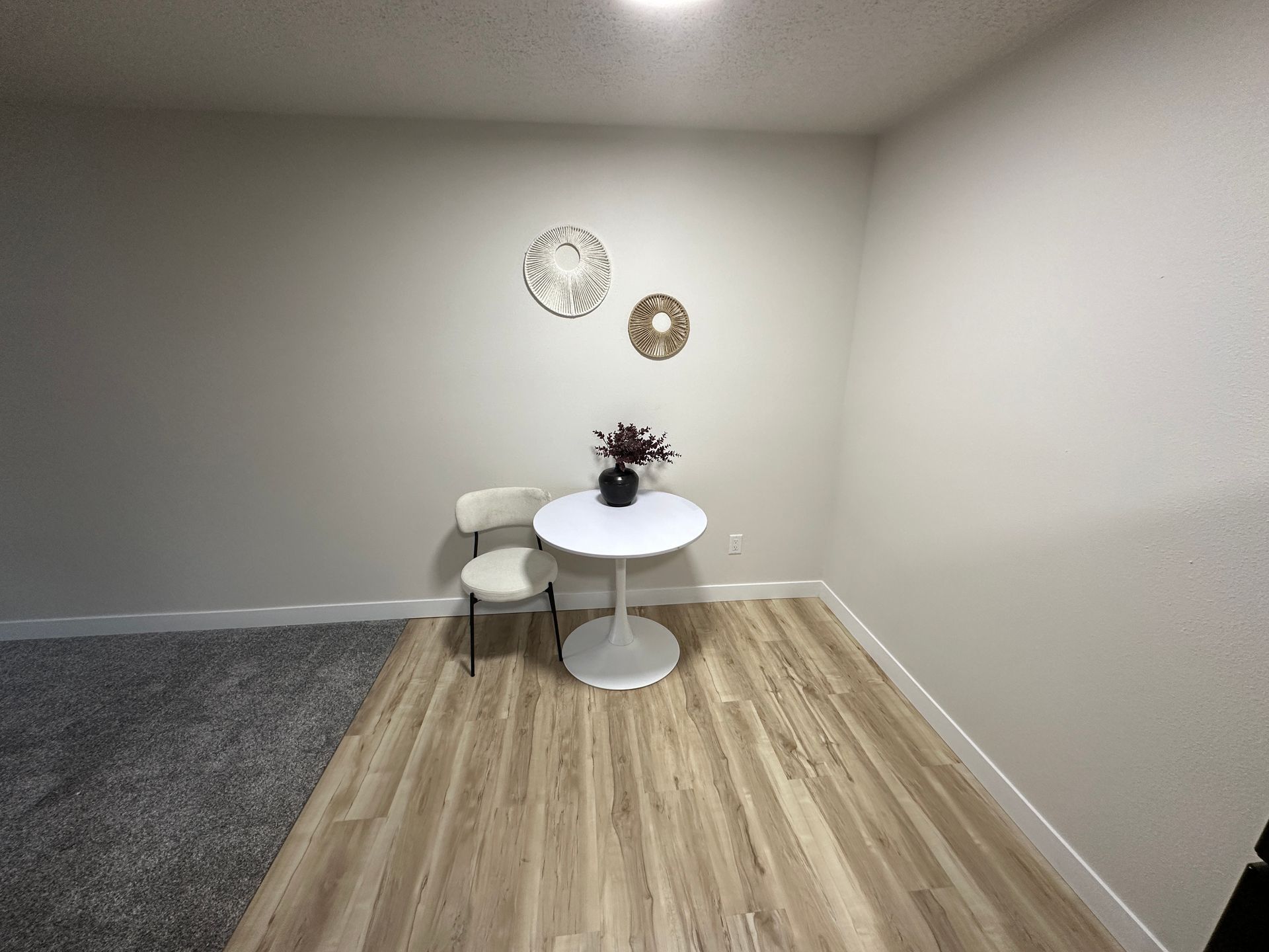 A small table and chair in a room with a clock on the wall.