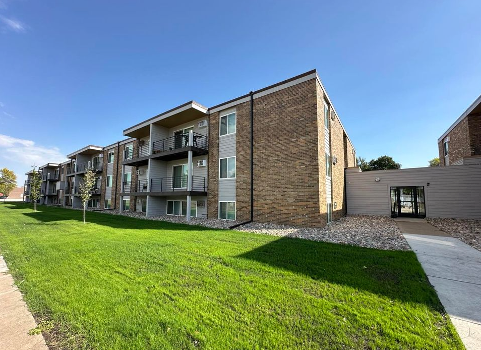 A large apartment building with a lush green lawn in front of it.