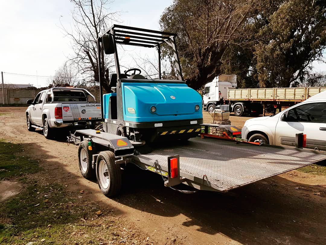 Una carretilla elevadora azul está siendo remolcada por un camión sobre un remolque.