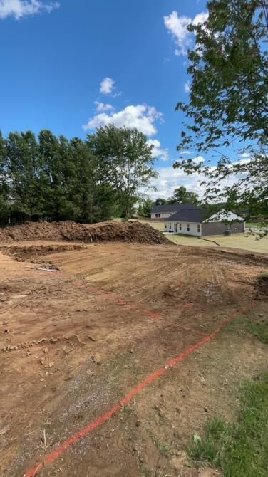 Construction site with freshly turned soil. A house is visible in the distance under a blue sky.