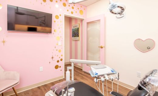 A bright, pastel-colored lobby featuring a white reception desk, pink striped walls, and a floral balloon arch.
