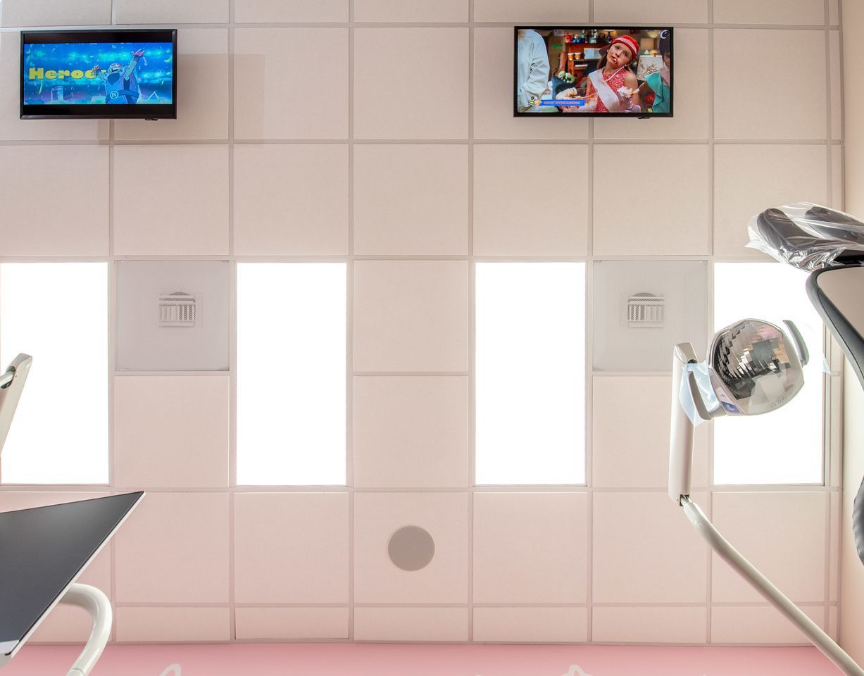 Child in a pink dental chair watches a screen in a colorful dental office.